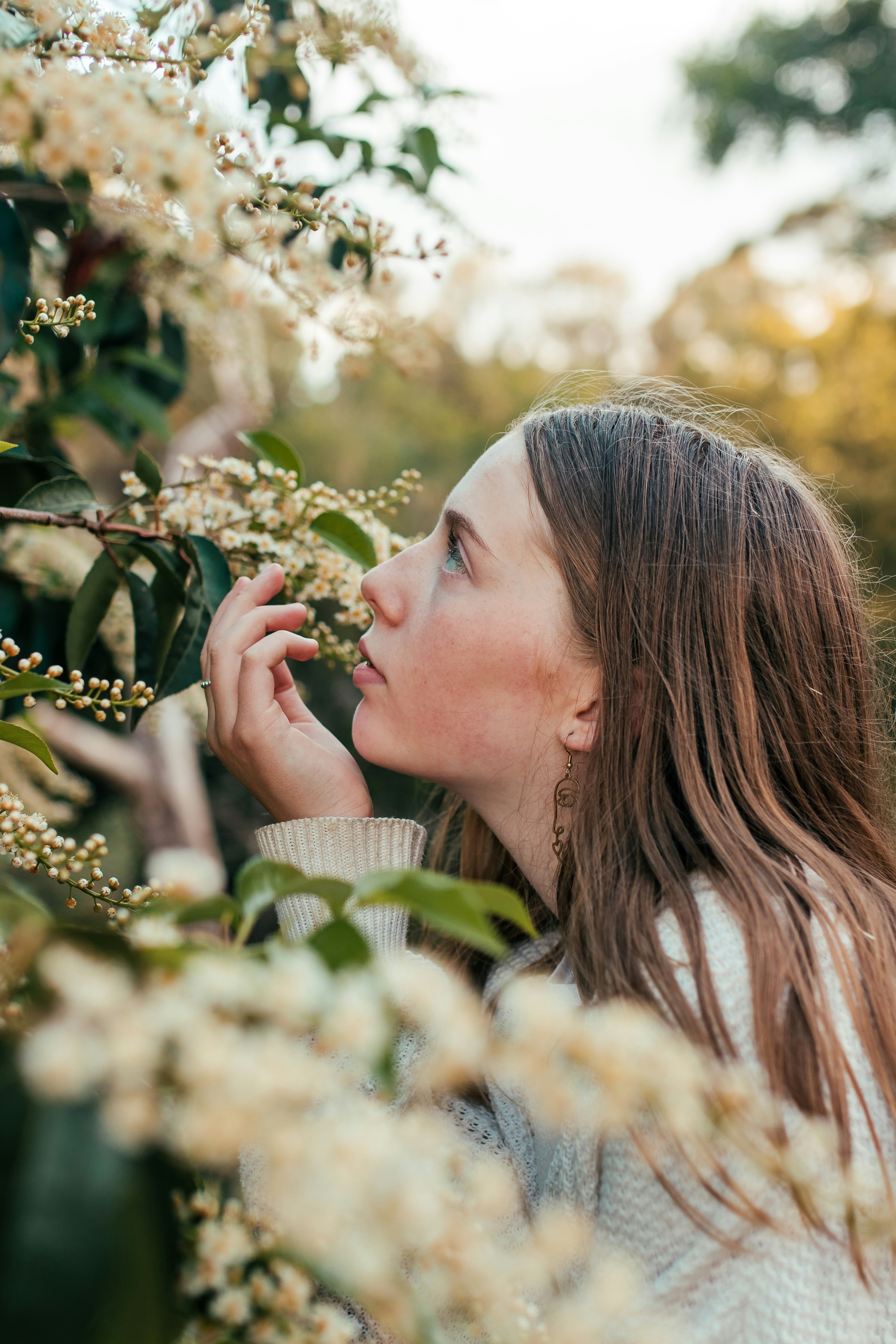 woman wearing white sweater smelling white flowers